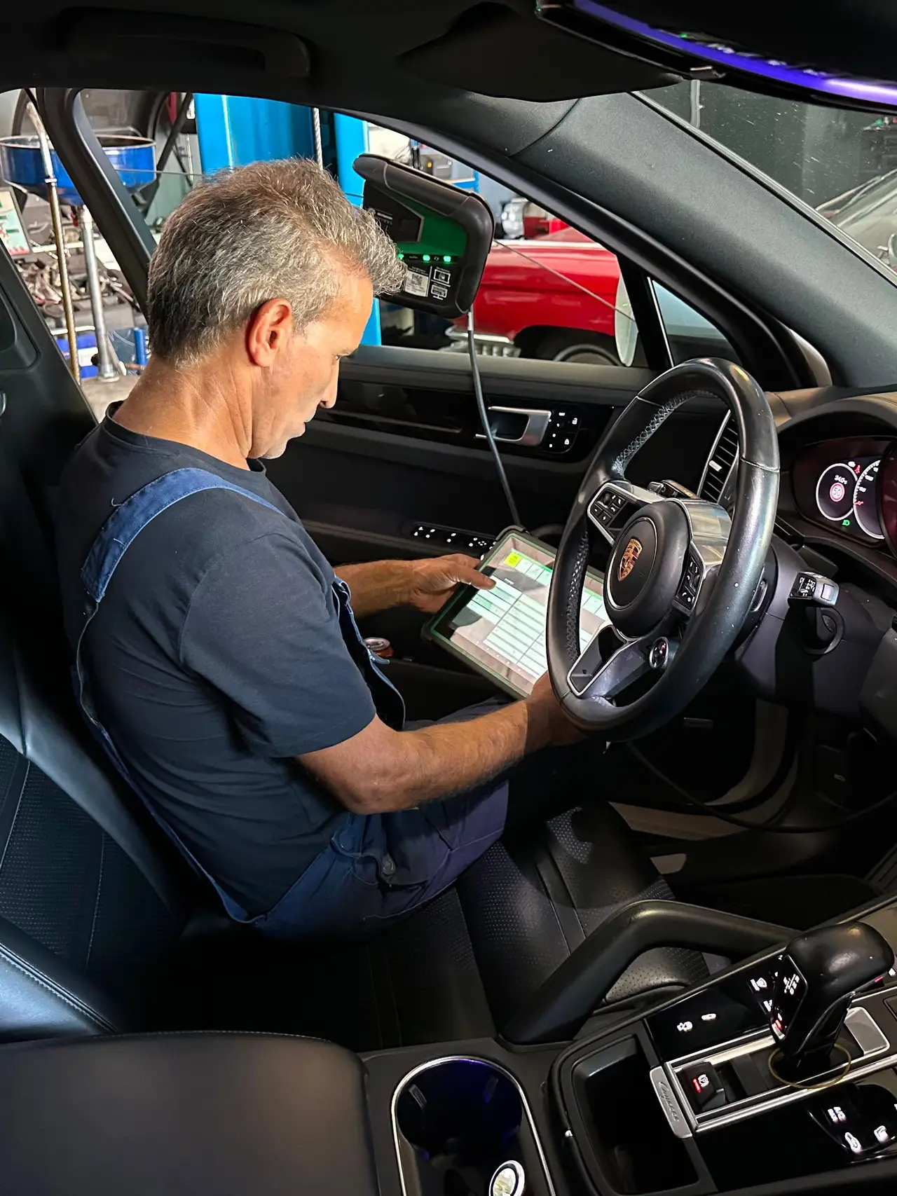Ein Mechaniker sitzt am Steuer eines Fahrzeugs und liest mit einem Tablet den Fehlerspeicher aus.